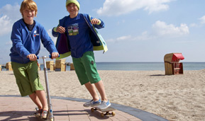 Jungs am Strand auf Roller und Skateboard mit Zahnspangen