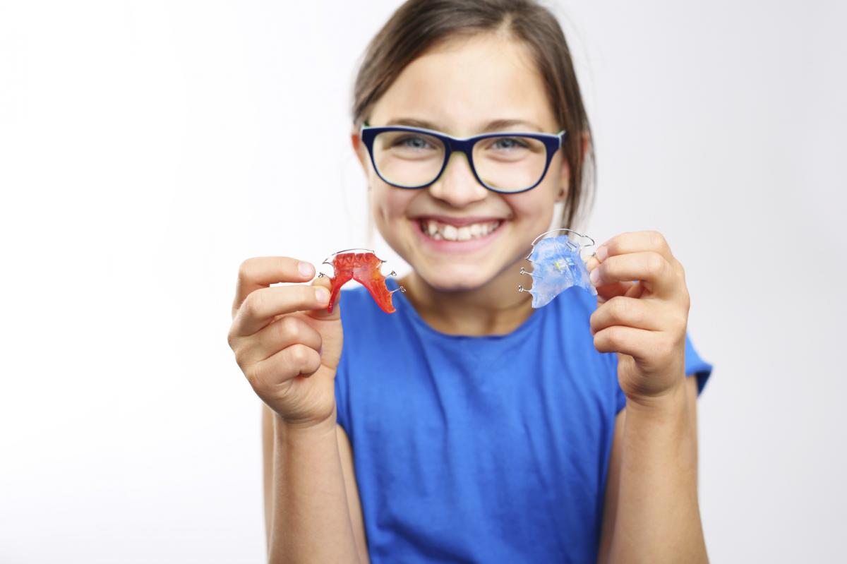 Mädchen mit Brille zeigt fröhlich zwei Zahnspangen in die Kamera